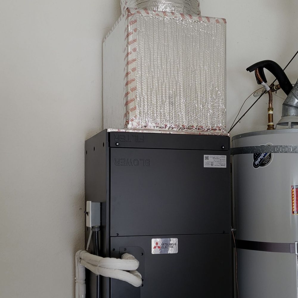 Mitsubishi Electric indoor air handler installed in a garage beside a water heater with an insulated plenum above it