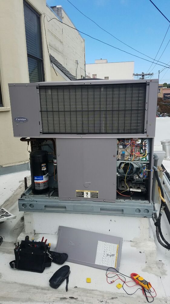 Carrier rooftop package unit opened for service with a multimeter and tool bag on the roof deck